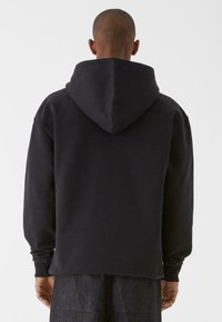 Fekete kapucnis pulóver, puha anyagból készült, hosszú ujjakkal és laza szabással. A kapucni nagy, és kényelmesen illeszkedik a nyakra.