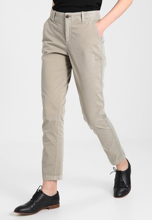 Pantalon beige à jambes droites porté avec des chaussures en cuir noires à lacets, visible de la taille aux pieds sur un fond uni.