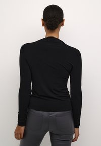 Schwarzes Langarmshirt mit figurnahen Design und Rippdetails an den Handgelenken, kombiniert mit grauen, enganliegenden Hosen. Schlicht und elegant.