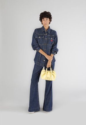 Jeansjakke med sølvknapper og to forlommer, parret med udvidede jeansbukser. Gul læderhåndtaske med sammenfoldet design.
