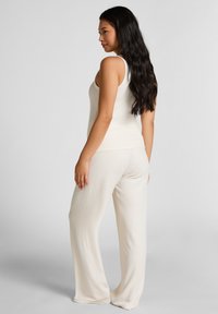 Crème-kleurige geribde gebreide tanktop gecombineerd met wijde broek, die een zachte textuur en een relaxte pasvorm toont. Zichtbare zijnaaddetails.
