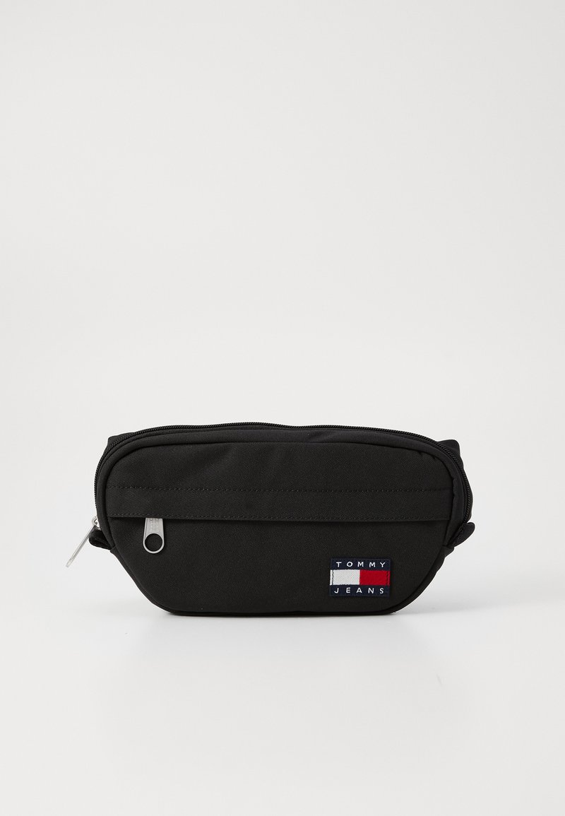 Zwarte stoffen pouch met een ritssluiting, voorzien van een voorvak en een klein multikleurig "TOMMY JEANS" logo patch. Compact en duurzaam ontwerp.