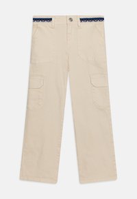 Pantaloni cargo beige con vestibilità ampia, dotati di due tasche laterali e una fascia decorativa in navy e rosso. Materiale in cotone, texture liscia.