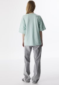 Mentolově zelené oversized tričko s krátkými rukávy, spárované se světle šedými džíny s kruhovými vzory a volným střihem.
