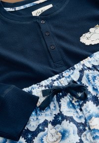 Námornícky pruhovaný pyžamový top s tromi gombíkmi, skombinovaný s modrými pyžamovými nohavicami so vzorom hravých karikatúr a s pásom na šnurovanie.