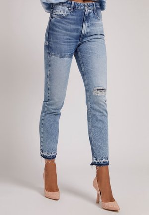 Lyseblå jeans med høj talje og lap-patch-design, knærevne med frynsete kanter, båret med nøgne spidse høje hæle.