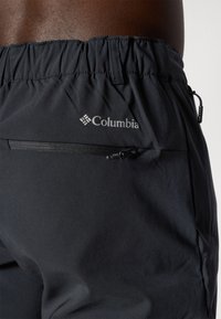 Czarne, lekkie szorty z elastycznym pasem, z zamkiem błyskawicznym i logotypem Columbia po lewej stronie. Gładka tekstura, oddychający materiał.