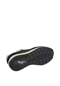Black sneaker with a textured rubber sole, featuring a white logo and subtle gray accents. Suede and textile materials present on the upper.
