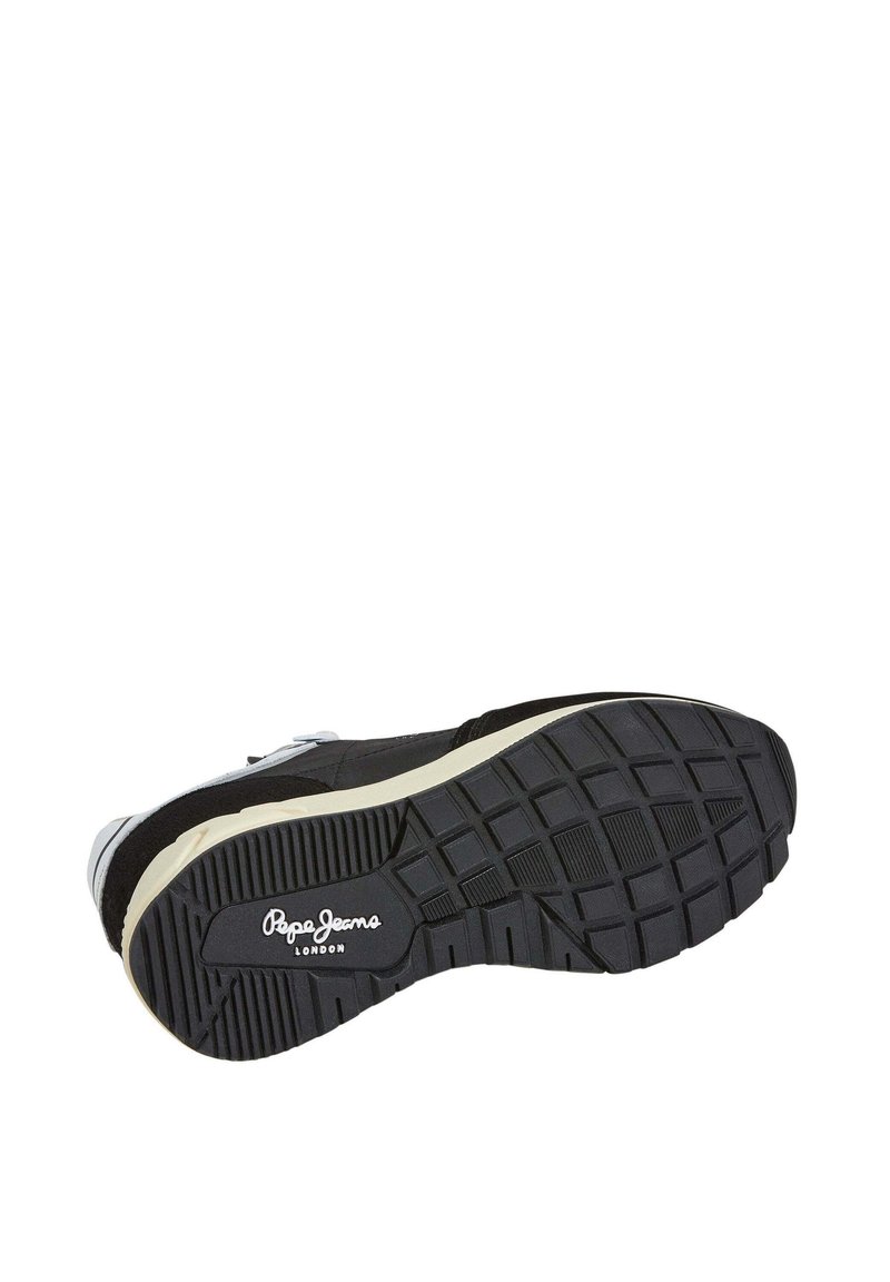 Zapatilla negra con suela de goma texturizada, que presenta un logo blanco y sutiles acentos grises. Materiales de ante y textil en la parte superior.