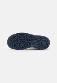 Svart Nike-sulas botten med cirkulära och linjära mönster, sedd uppifrån mot en vit bakgrund.