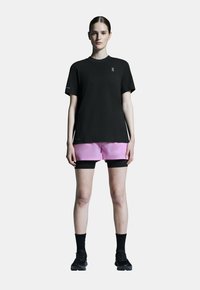 Schwarzes T-Shirt mit kurzen Ärmeln, kombiniert mit rosa Shorts und schwarzen Sportstrümpfen und Schuhen. Einfaches Design, keine sichtbaren Muster oder Verzierungen.