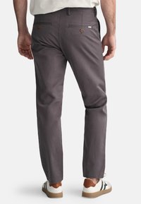 Grijze broek met een rechte snit, voorzien van twee achterzakken die zijn beveiligd met bruine knopen en een subtiele gemêleerde stof. Gecombineerd met witte sneakers.