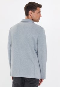 Szary blezer z miękkiego materiału, z kołnierzykiem, tylnymi szwami i bocznymi kieszeniami. Charakteryzuje się luźnym krojem i minimalistycznym stylem.