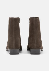 Bottines en daim marron avec une texture lisse, un bout arrondi et un petit talon empilé. Elles disposent d'une fermeture éclair sur le côté pour un enfilage facile.