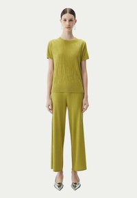 Olivgrön kortärmad topp med strukturerad mönstring, kombinerad med ribbade vida byxor, kompletterad med metalliska silverfärgade spetsiga skor.