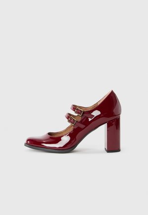 Burgundy patent leather high heel shoe with rounded toe, two adjustable buckle straps, and a chunky block heel. Smooth texture throughout.