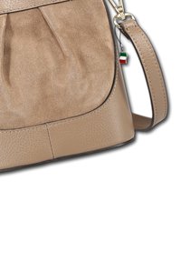 Beige leren handtas met geplooid ontwerp, gladde textuur en een contrasterende donkere basis. Voorzien van een korte schouderband en een klein Italiaans vlaggetje charm.