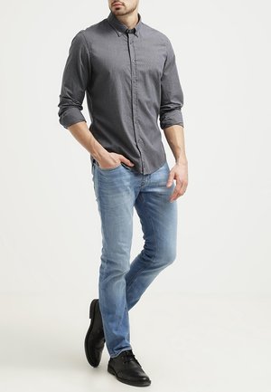 Harmaa nappipaita hienovaraisella kuviolla, yhdistetty vaaleansinisiin farkkuihin ja mustiin pukukenkiin, luo rentoon mutta siistiin ilmeeseen.