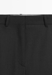 Zwarte op maat gemaakte broek met een gladde textuur, een platte voorkant en subtiele stikdetails. Inclusief riemlussen en een verborgen rits.