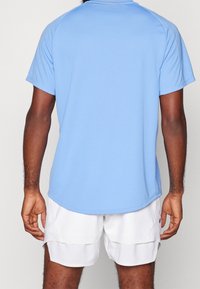 Ljust blå idrottströja i ett slätt tyg med korta ärmar, med rundad nederkant, bära med vita shorts. Inga anmärkningsvärda logotyper närvarande.