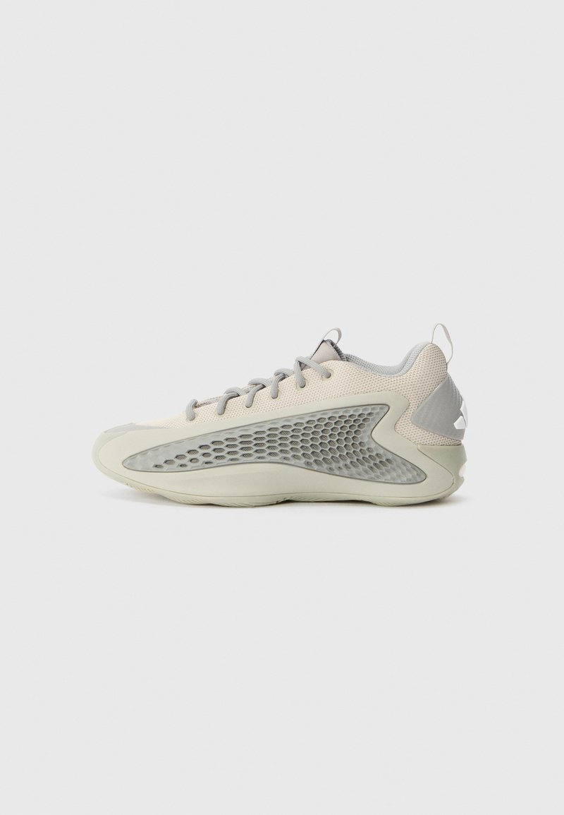 Ljusgrå sneaker med en strukturerad meshuv, distinkta sidoventiler och en vit gummisula. Har platta skosnören och en dragflik vid hälen.