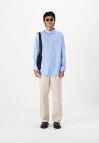 Lyseblå stribet skjorte med knapper, beige bukser, sort taske og sorte sko. Skjorten har en afslappet pasform og krave.
