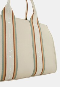 Witte tas met structuur en twee-kleurige stoffen handvatten, voorzien van verticale strepen in bruin, groen en crème met "Armani Exchange" branding.