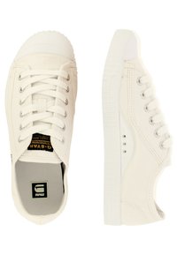 Baskets en toile blanches avec un embout en caoutchouc, design à lacets et semelle texturée. Présente un logo noir et or sur la languette.