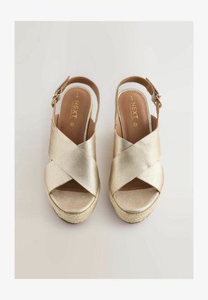 Guld syntetiske slingback sandaler med krydsremdesign, espadrille-lignende jute-sål og justerbart spænde. Glat tekstur og polstret indersål.