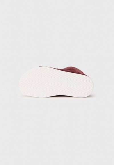 Burgundia värvi sametiste sneakerite valge kummist põhi, millel on siksakilised mustrid. Disain hõlmab ümarate servadega vormi ning nähtavat brändingut pole.