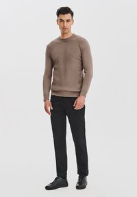 Beżowy sweter z teksturowanym splotem, długie rękawy, okrągły dekolt, sparowany z czarnymi spodniami i czarnymi trampkami. Prosty, dopasowany krój, minimalne akcenty.