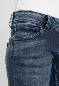 Jeans in denim blu scuro con un classico design a cinque tasche, lievi dettagli sbiaditi e una vita standard con passanti per cintura.