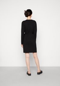 Svart klänning med långa ärmar, figursydd midja och rak skärning, tillverkad av mjukt tyg. Har rund halsringning och sidofickor.