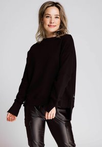 Schwarzer übergroßer Sweatshirt mit langen Ärmeln und gerippten Bündchen, kombiniert mit schwarzen Faux-Lederhosen mit Cargo-Taschen und Kordelzugbund.