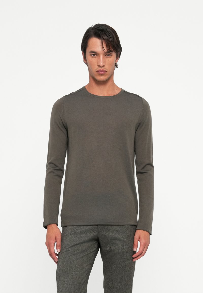 Long-sleeve, round-neck shirt in dark olive green fabric, featuring ribbed texture and solid design, paired with gray patterned trousers.