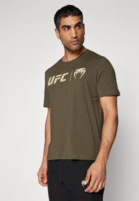 Oliven grøn t-shirt med korte ærmer lavet af bomuld, med hvidt UFC-logo og slangegrafik på forsiden. Rund hals og almindelig pasform.