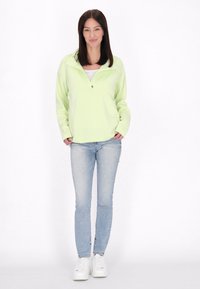 Pullover verde chiaro con colletto a mezza zip, maniche lunghe, abbinato a jeans azzurri e sneaker bianche. Tessuto morbido, vestibilità rilassata.