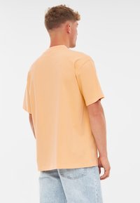 Korte mouwen T-shirt in zacht perzik stof, met een relaxte pasvorm en ronde hals. De achterkant toont een eenvoudig, naadloos ontwerp.
