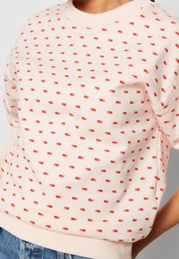 Felpa rosa chiaro con un piccolo motivo di bandierine rosse, collo e polsini a costine, vestibilità rilassata, realizzata in tessuto morbido. Stile casual, senza texture evidenti.