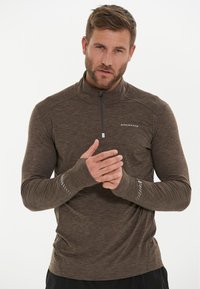 Brun, langærmet halv-zip skjorte med en struktureret overflade, der har reflekterende detaljer på manchetterne og et logo på brystet.