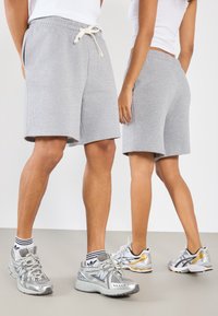 Shorts en coton gris avec taille élastique et cordon de serrage. Deux modèles portent des chaussures de sport coordonnées et des chaussettes à motifs.