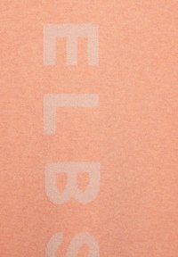 Pfirsichfarbener Stoff mit weicher Textur, der große, helltönige Buchstaben enthält, die in einem subtilen, tonalen Muster bedruckt sind.