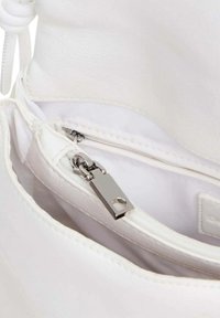 Interno di una borsa in pelle bianca con una tasca con zip dotata di zipper argentato e una fodera in tessuto liscio. Sono visibili cuciture dettagliate.