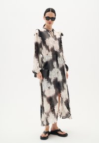 Vestido midi floral en tonos negro, blanco y rosa pálido con pliegues verticales. Cuenta con mangas largas, un escote en forma de ojo de cerradura y una abertura lateral.