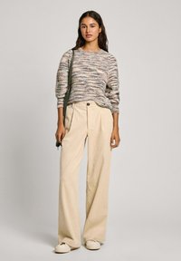 Knit sweater with multicolored horizontal stripes, paired with beige wide-leg textured trousers and light shoes. Simple strap bag across the body.