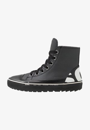 Zapatilla negra alta con tejido texturizado, puntera de goma y suela gruesa. Presenta cordones negros y un logotipo blanco en contraste en el costado.