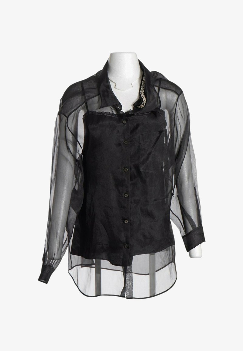 Blouse noire transparente à manches longues avec boutonnage à l'avant et un caraco noir uni en dessous, superposé sur un mannequin blanc.