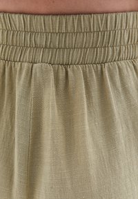 Licht olijfgroene rok met een smocked tailleband, een vloeiende textuur en zacht, lichtgewicht stof met een subtiele glans en natuurlijke kreuken.
