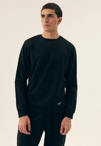 Czarna bluza z miękkiego, teksturowanego materiału. Posiada okrągły dekolt, długie rękawy i mały detal z logo na dole.