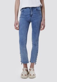 Jeans de mezclilla azul claro con cintura alta, ajuste slim y largo recortado; cuentan con detalles de botones a lo largo del dobladillo y una textura suave.